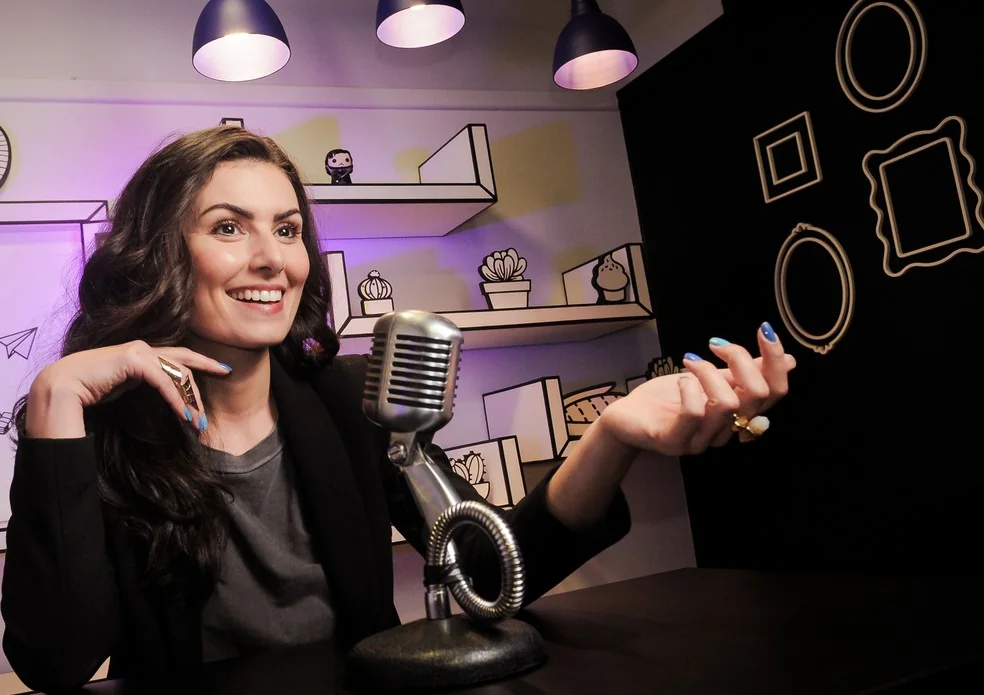 Nathalia Arcuri falando com expressão e gestos diante de um microfone no estúdio Me Poupe